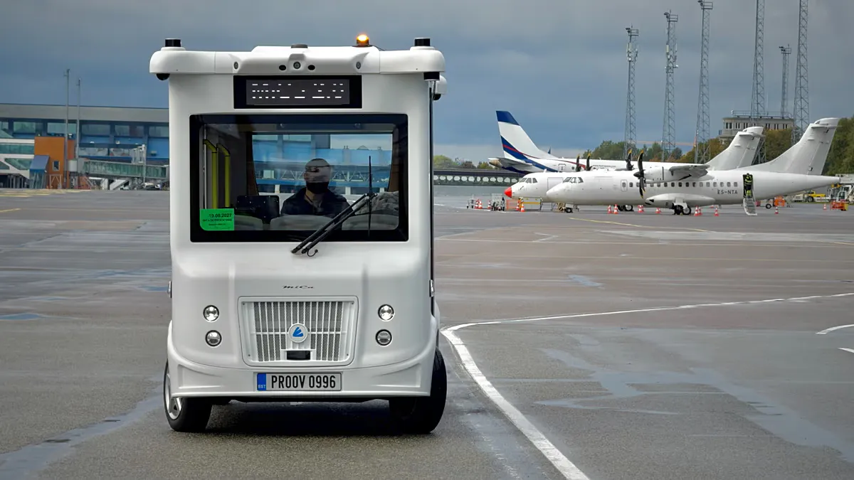 An electric shuttle on an airport service road near aircraft hangars